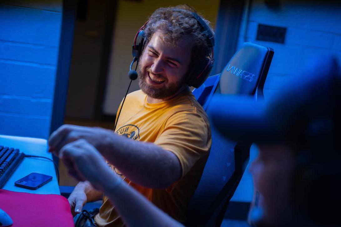 Two Kettering E-sports players smile and fist bump one another. One student wears a gaming headset.